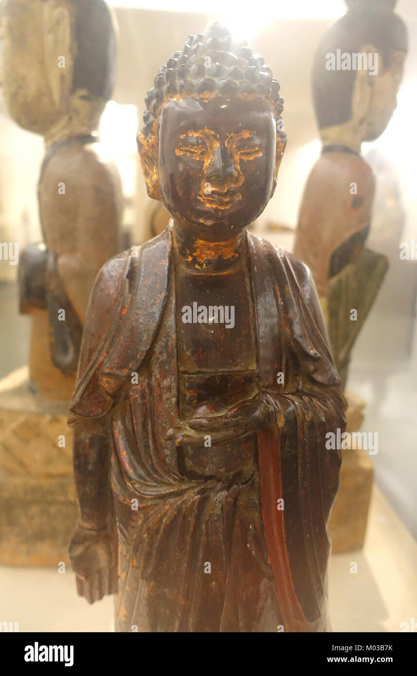 Eine hölzerne Skulptur von Buddha, der auf einem Lotusthron steht, ausgestellt im Vietnam National Museum of Fine Arts in Hanoi. Dieses Artefakt zeigt die Handwerkskunst der vietnamesischen Holzschnitzerei und der buddhistischen Kunst und spiegelt die religiöse und kulturelle Bedeutung des Buddhismus in Vietnam wider. Die Skulptur ist ein bedeutendes Stück in der Sammlung des Museums. Stockfoto