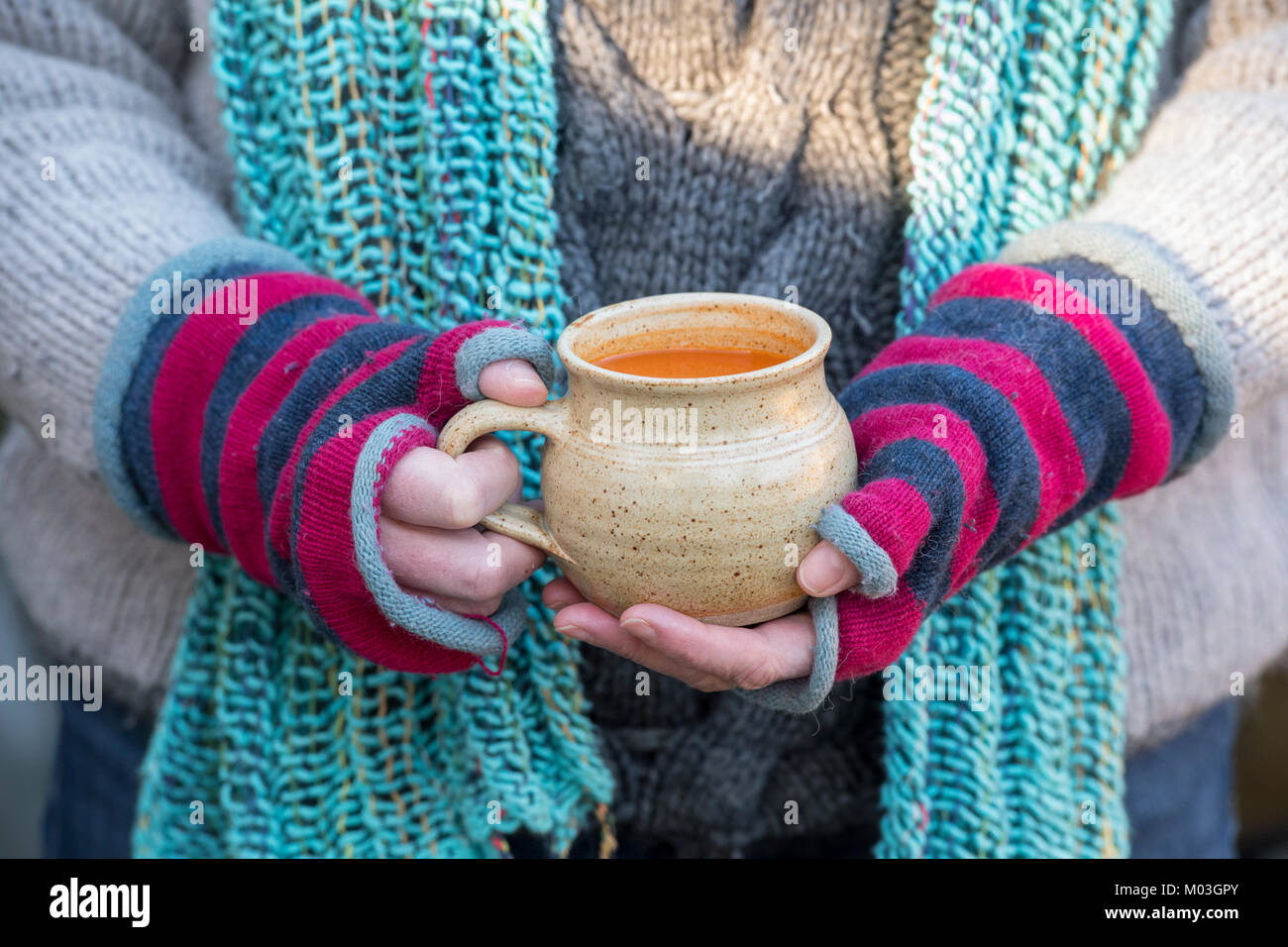 Frau tragen bunte Wolle fingerlose Handschuhe halten einer Tasse Tomatensuppe im Winter. Großbritannien Stockfoto
