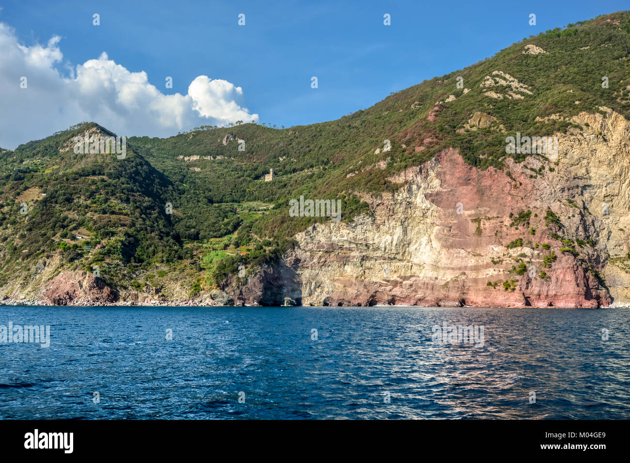 Die farbenfrohen roten Felsen an der ligurischen Küste von Italien zwischen Cinque Terre und Portovenere mit einer Burg oder Palazzo hoch auf einem Hügel Stockfoto