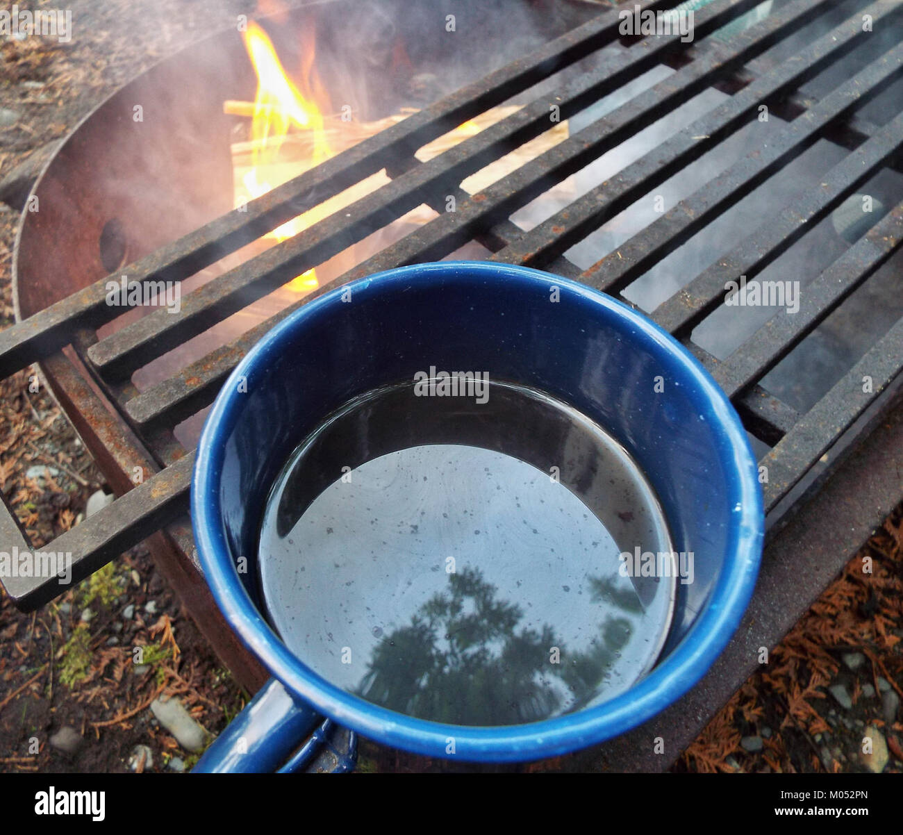 Dieses Foto zeigt den Prozess der Kaffeezubereitung über einem Lagerfeuer, eine Methode zur Kaffeezubereitung im Freien, die häufig mit Camping- und Outdoor-Aktivitäten assoziiert wird. Es unterstreicht eine rustikale und traditionelle Brautechnik. Stockfoto