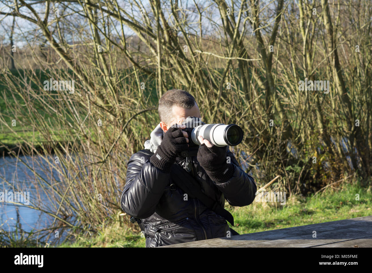 Professioneller männlicher Naturfotograf, der am kalten Wintermorgen in Großbritannien fotografiert. Stockfoto