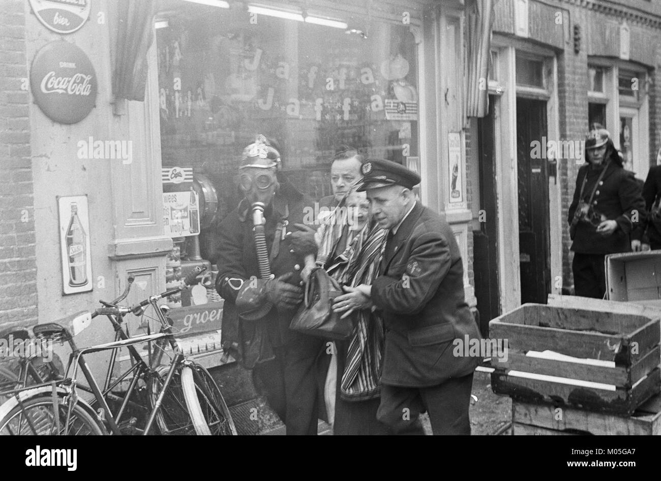 Dieses historische Foto zeigt eine Szene in Jacob van Campenstraat mit einer älteren Frau, die während eines Brandfalls von Feuerwehrleuten umgeben ist. Das Bild bietet einen anschaulichen Einblick in das Leben während des frühen 20. Jahrhunderts in den Niederlanden. Stockfoto