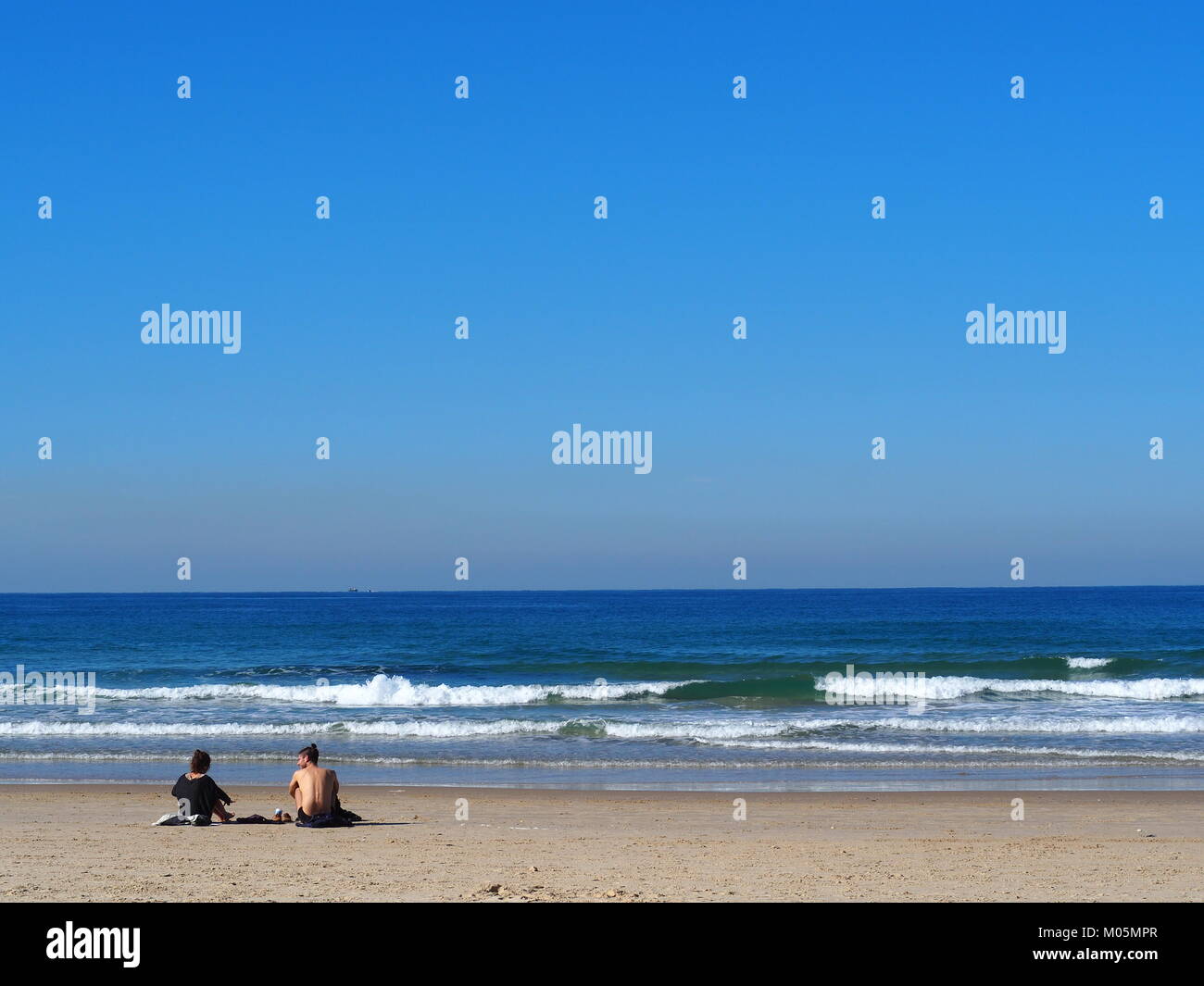Zwei Freunde sitzen am Strand Sand auf einem perfekt klaren Tag und ein Gespräch mit jeder anderen Stockfoto