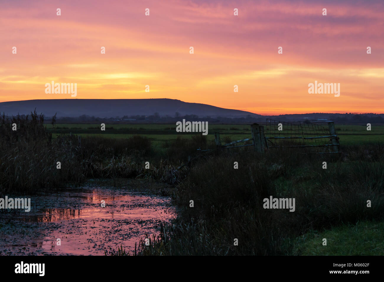 Sonnenuntergang in Wasser über Pevensey Levels mit der South Downs am fernen Horizont. Stockfoto