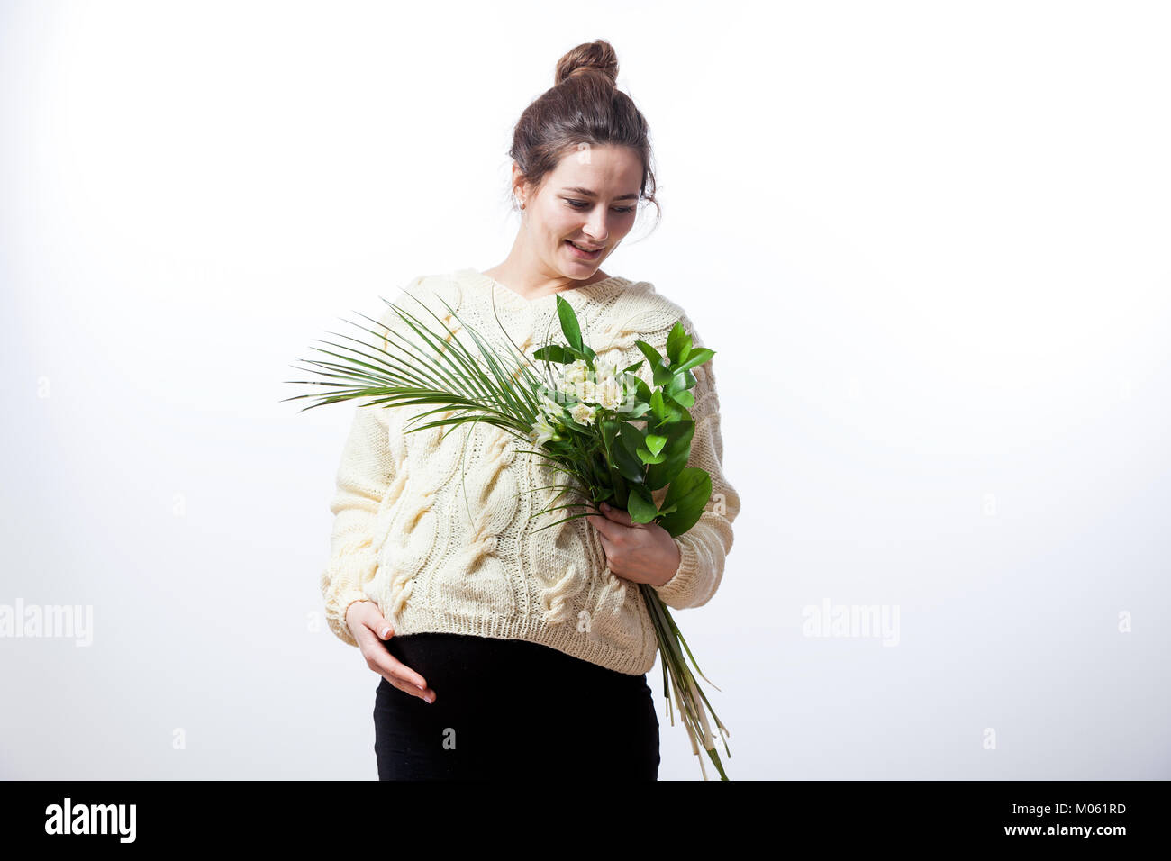 Junge fröhliche dunkelhaarige Frau in einem gestrickten Pullover und einem schwarzen Kleid auf Ihrem letzten Schwangerschaft hält einen Strauß Blumen der Blenden in ihren Händen, posin Stockfoto