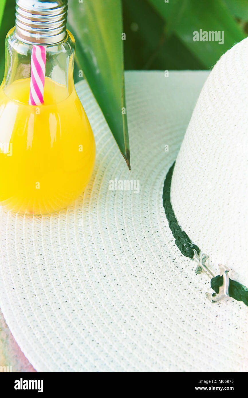 Glühlampe Glas Flasche mit frisch gepressten tropischen Früchten Saft Strohhut grüne Palmenblättern Laub Hintergrund gedrückt. Seaside Beach Ferienhäuser Stockfoto