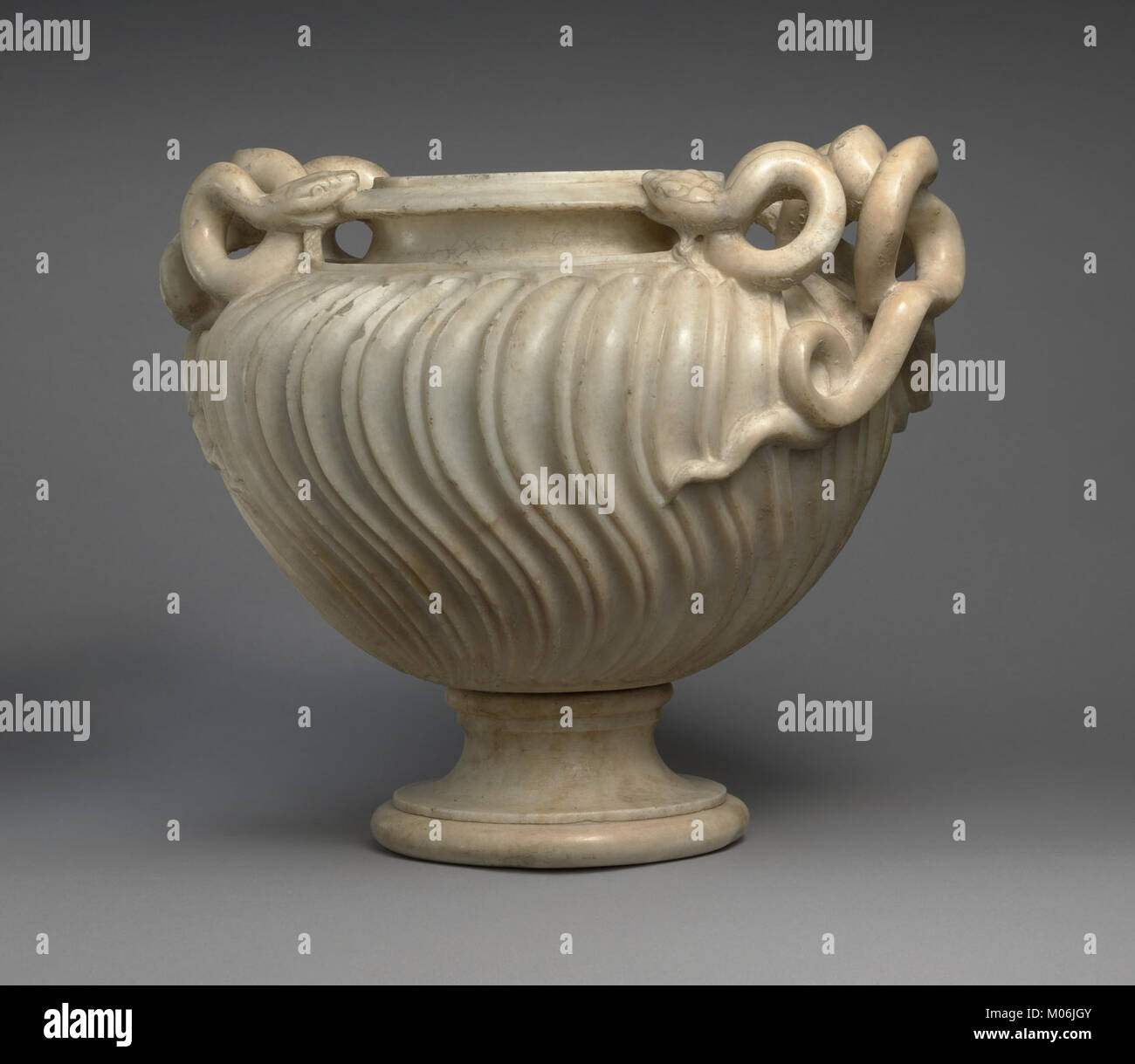 Die Marmorvase ist mit gestreiften Verzierungen und schlangenförmigen Griffen versehen, die Handwerkskunst und dekorativen Stil der klassischen Antike zeigen. Stockfoto