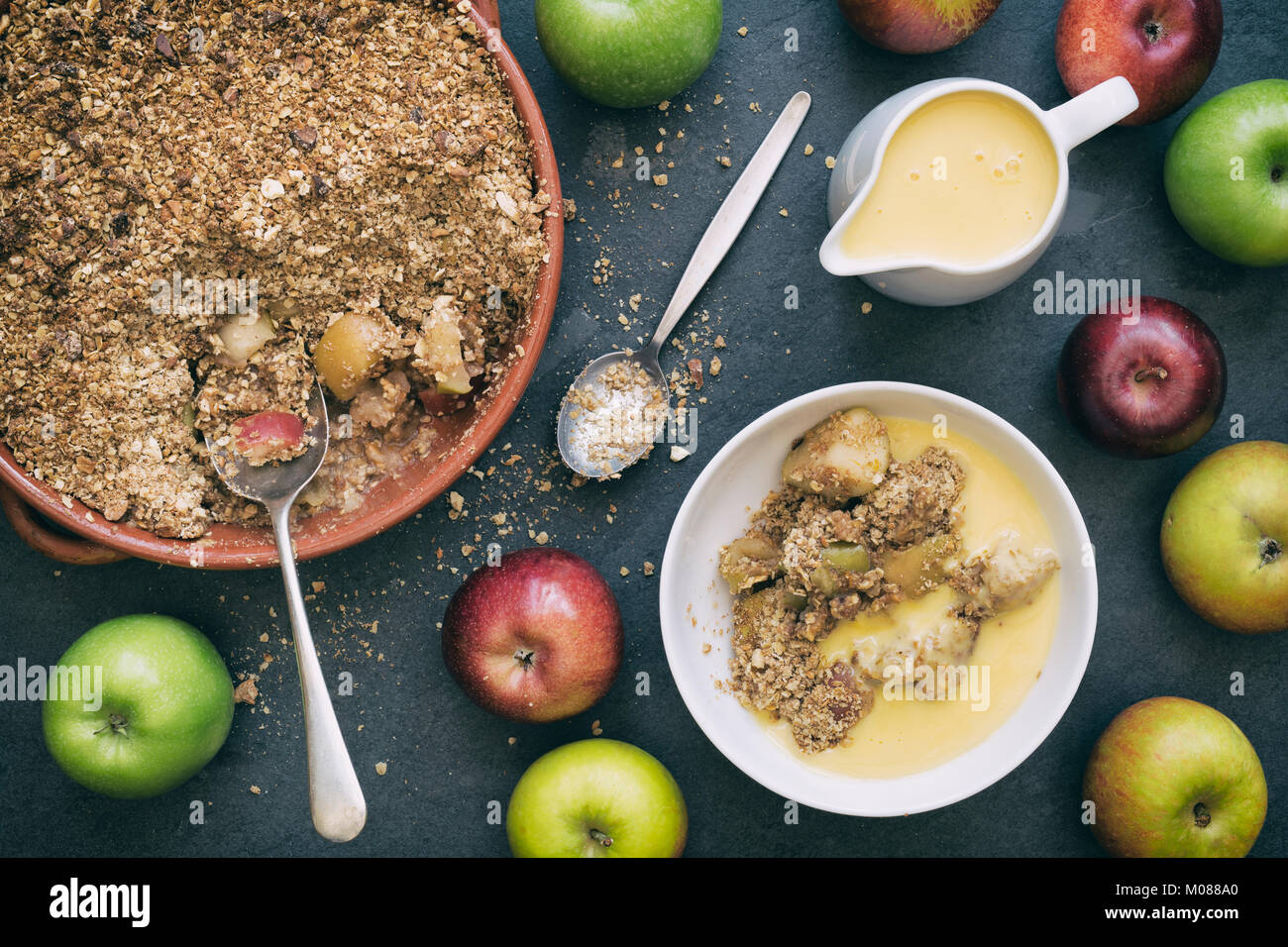 Apple Crumble, Pudding und frische Äpfel auf einer Schiefertafel Hintergrund Stockfoto