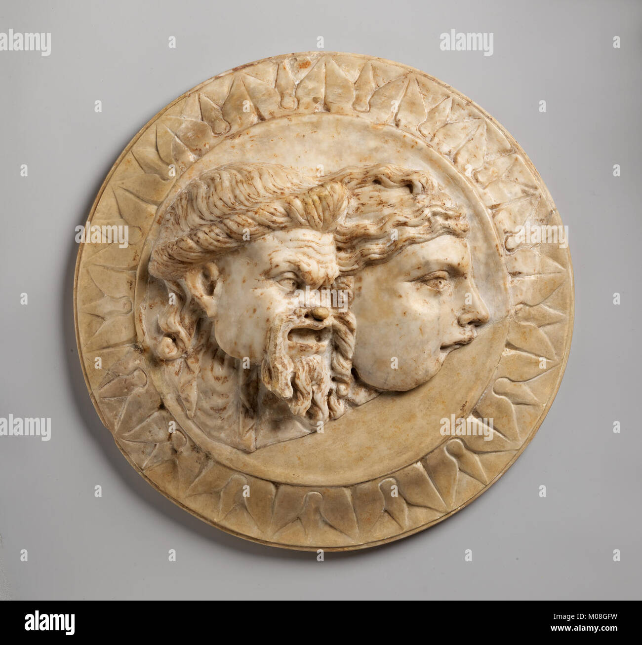 Diese Marmorscheibe zeigt zwei Theatermasken im Relief, die Schauspiel und Aufführung in alten Kulturen und künstlerischen Traditionen darstellen. Stockfoto