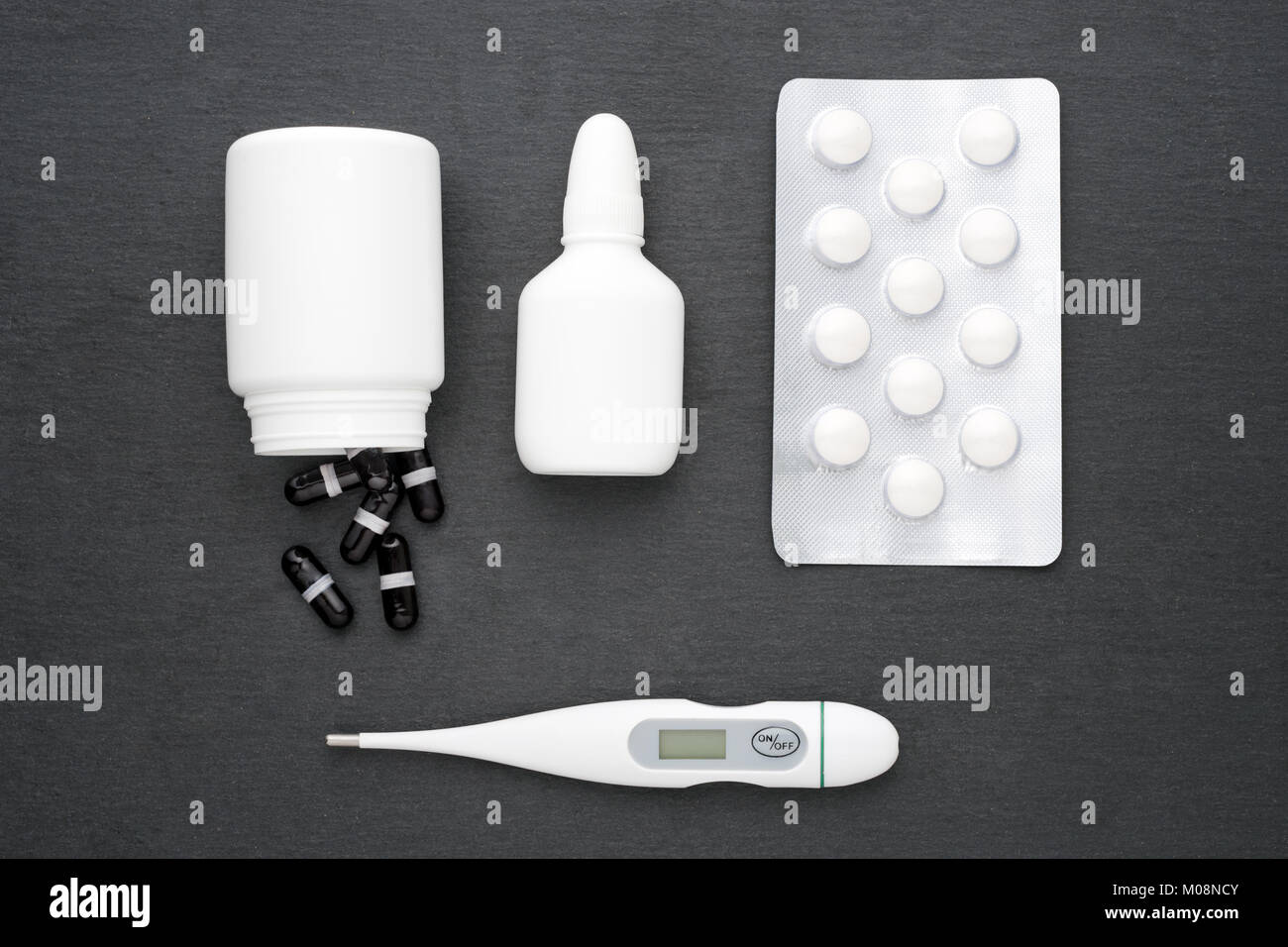Thermometer, Nasentropfen, Kapseln und Tabletten auf dunklem Schiefer. Flach. Medikamente für die Behandlung, Health Care Konzept Stockfoto