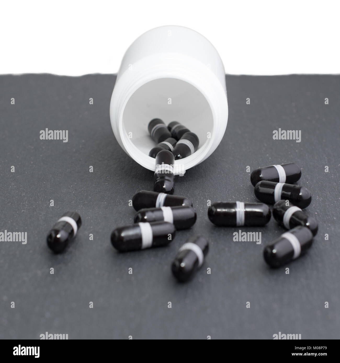 Schwarz Ergänzung Kapseln sind weiße Flasche auf schiefer Board gegossen. Medizin, Gesundheitswesen Konzept Stockfoto