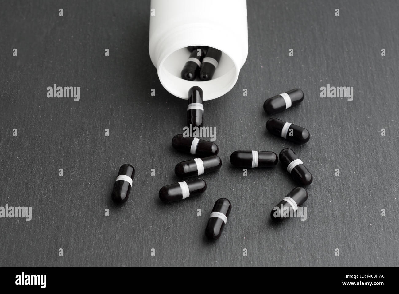 Schwarz Ergänzung Kapseln sind weiße Flasche auf schiefer Board gegossen. Medizin, Gesundheitswesen Konzept Stockfoto