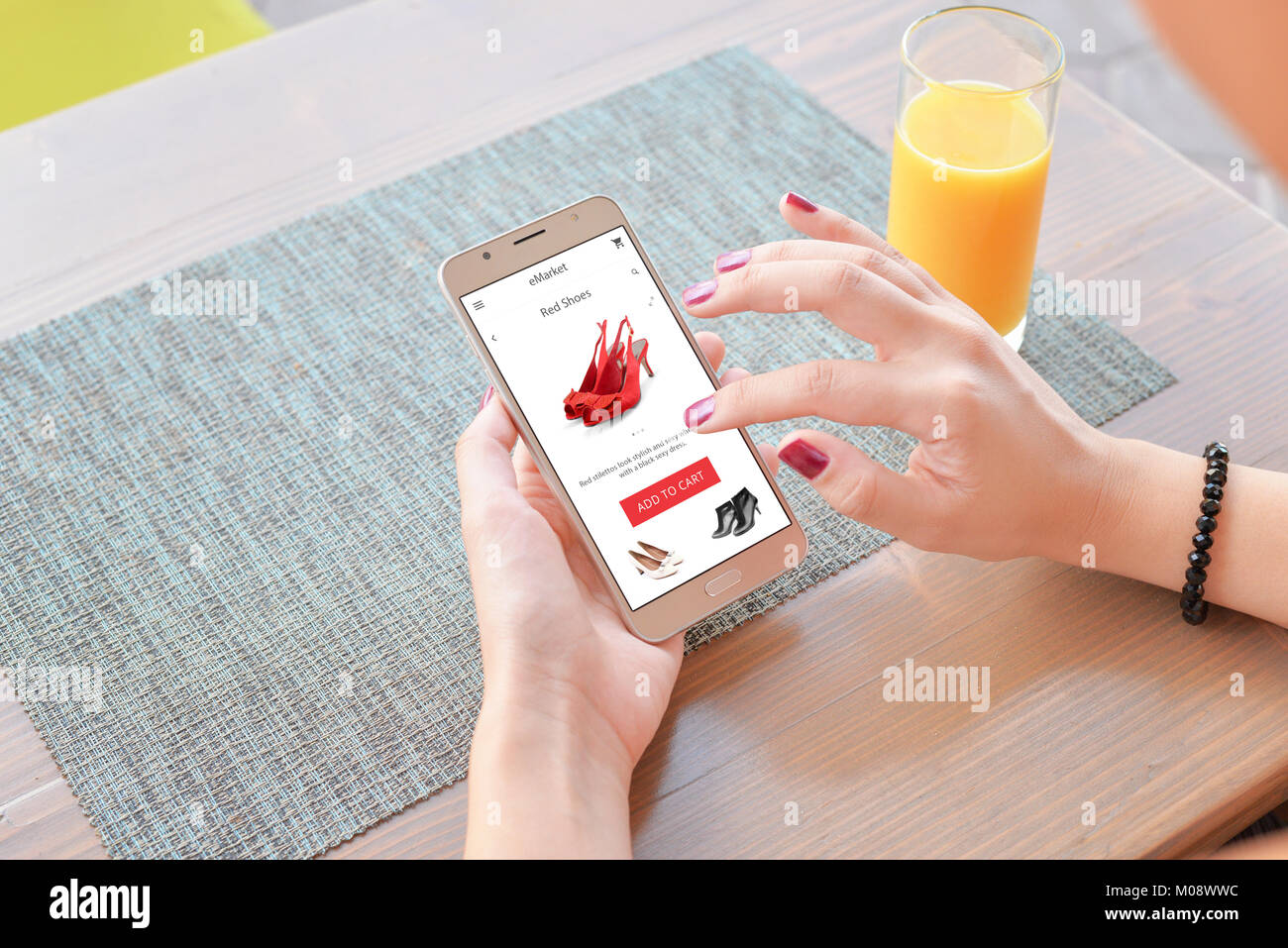 Frau Kaufen rote Schuhe online. Mobile App oder Website auf dem Bildschirm. Tabelle und Saft im Hintergrund. Stockfoto