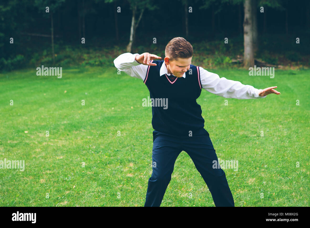 Ein Junge, Teenager, Schüler in formale gekleidet Imitiert ein Kampf vor einem Wald auf einer Wiese im Sommer. Stockfoto