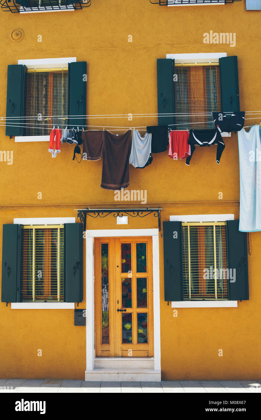 Senf Haus Wand mit Wäsche draußen hängen während der Nebensaison in Insel Burano, Venedig, Italien. Stockfoto