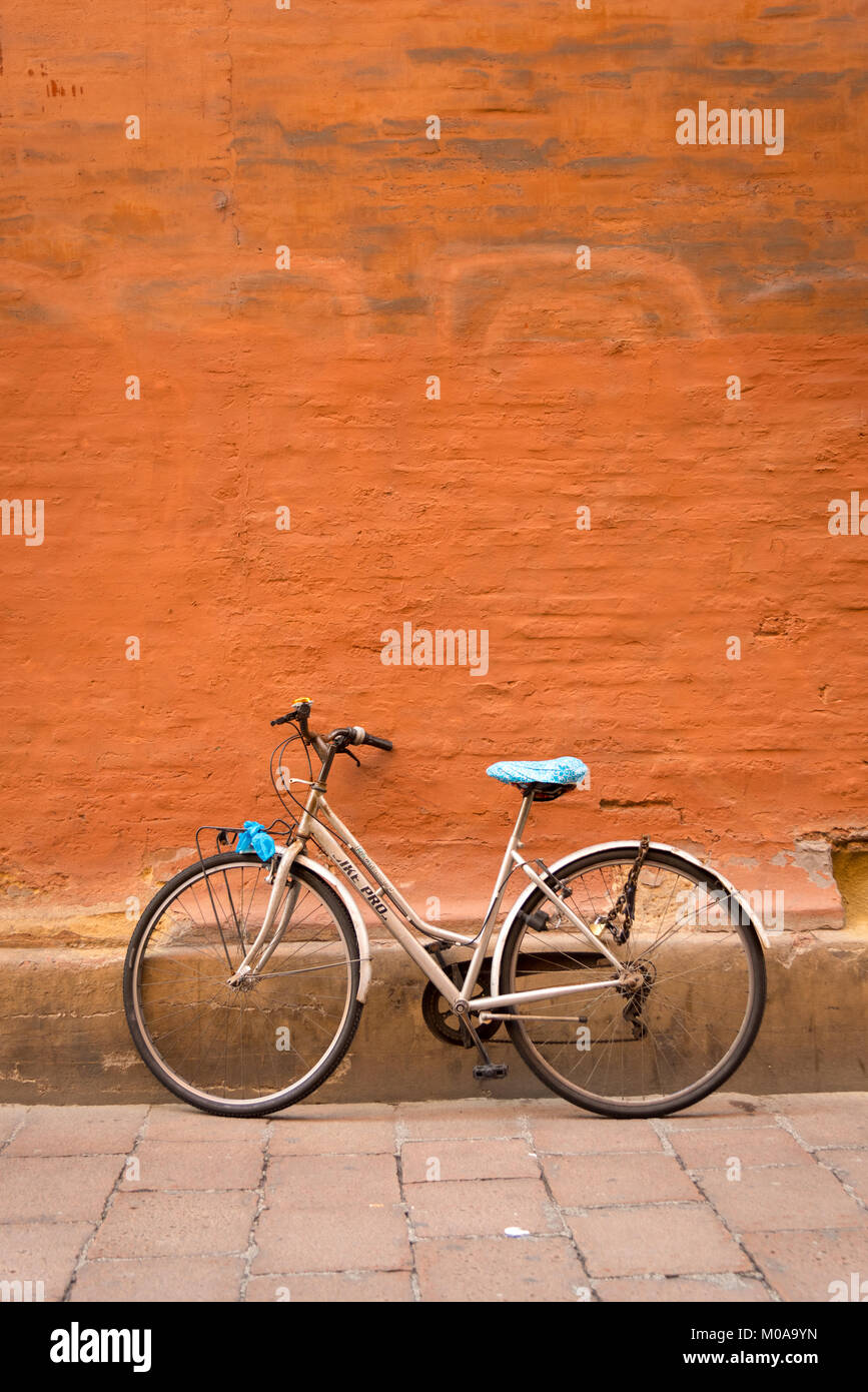 Ein Zyklus mit Kunststoff blau Sitz lehnte sich gegen eine bemalte terrakottafarbenen Wand in Bologna, Italien. Eine auffallende Farbe Bild. Stockfoto
