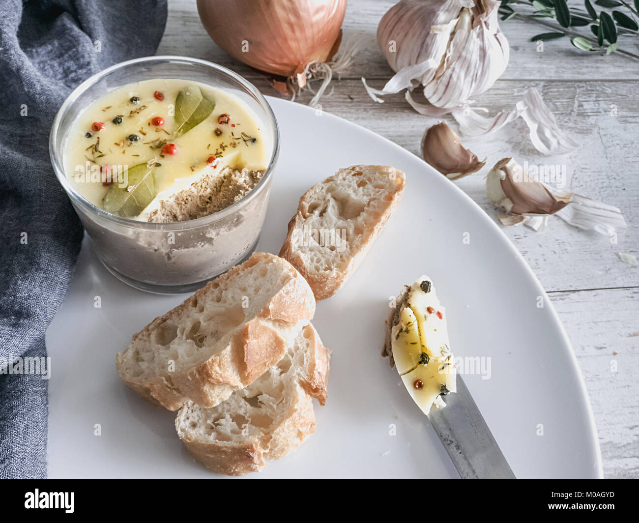 Frische hausgemachte Huhn Leber Pastete mit zerlassener Butter bedeckt und mit Lorbeerblättern und schwarzer und roter Pfeffer auf weiße Platte eingerichtet. Rustikal zurück Stockfoto