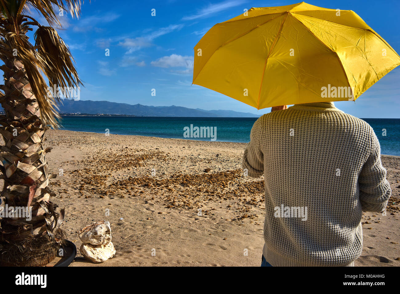 Mann auf einer mediterranen Sandstrand mit einem gelben Regenschirm an einem sonnigen Tag Stockfoto