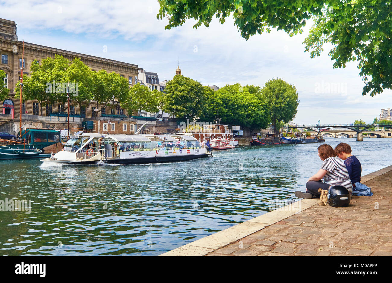 PARIS, Frankreich, 15. MAI 2017: Junge Menschen, die durch den Fluss Seine an der Spitze der Ile de la Cite Insel sitzen wie Fahrgastschiffe sie vorbei führen. Paris ist. Stockfoto