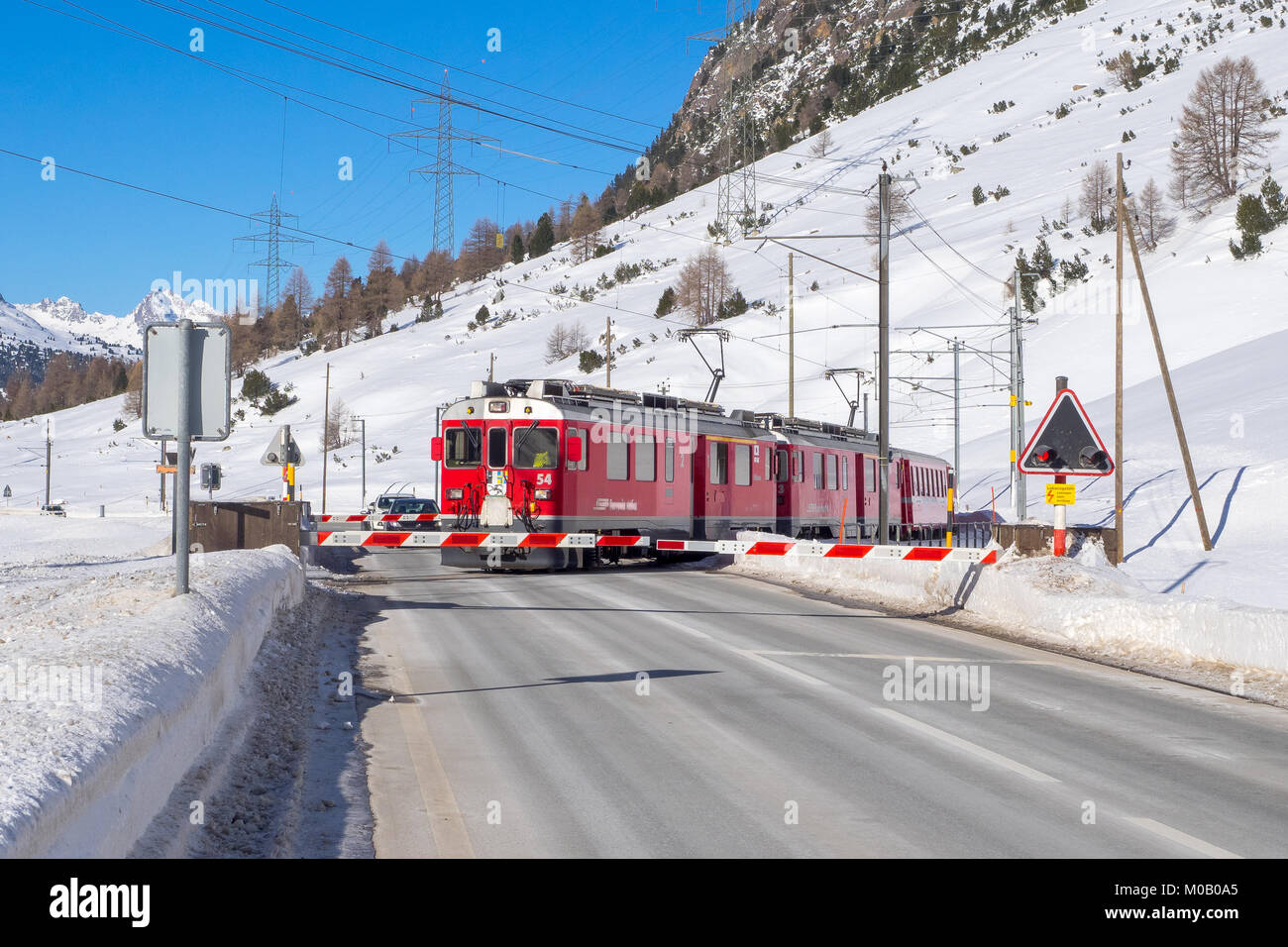 Red Train der Bernina führt über einen Bahnübergang im Winter Reise Stockfoto