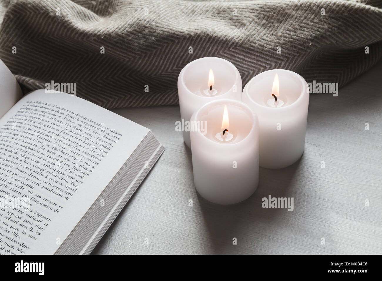 Gemütliche Kerzen und Buch mit Decke Stockfoto