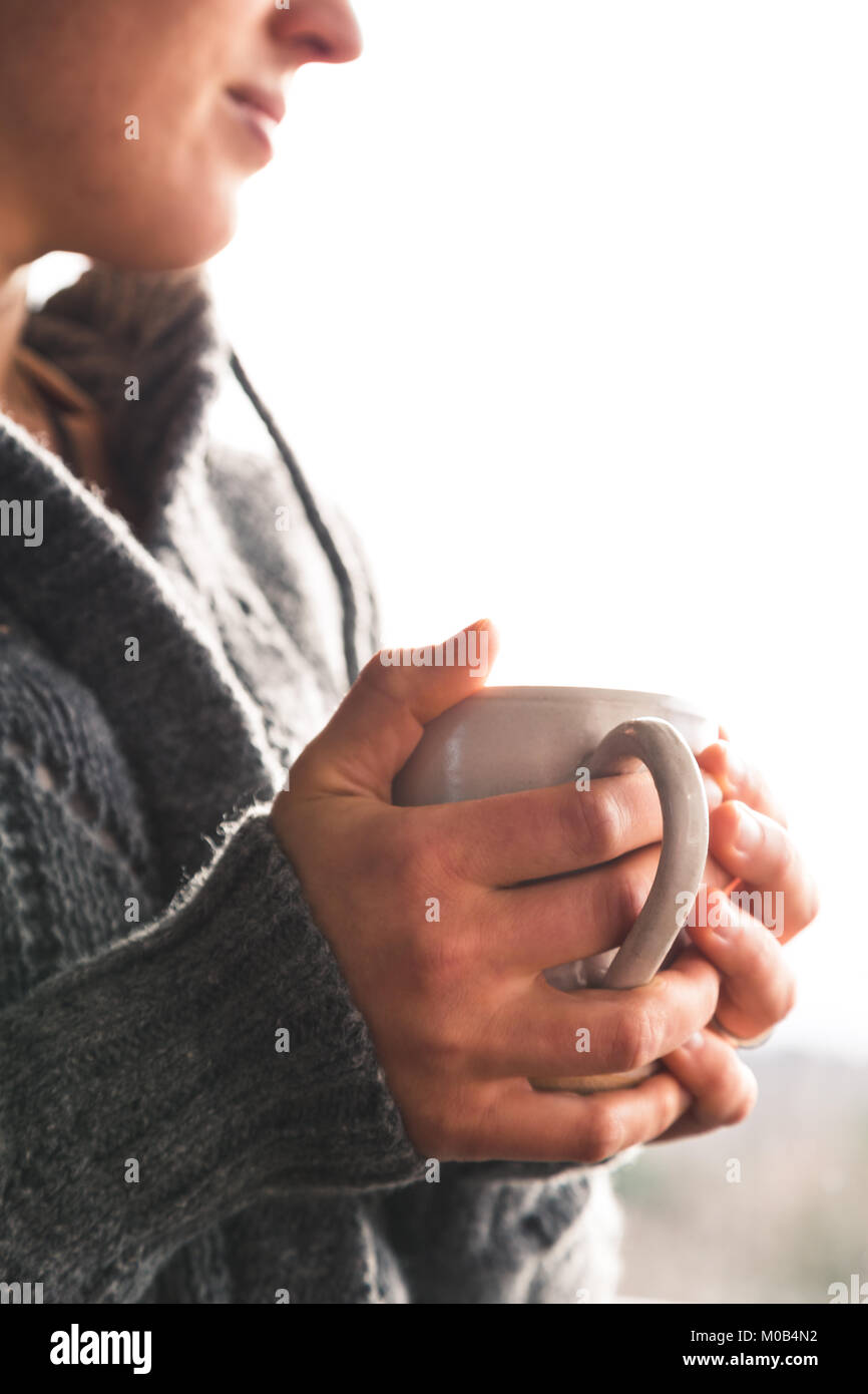 Frau mit Tasse Tee tragen graue Wollpullover Cardigan aus dem Fenster suchen Stockfoto