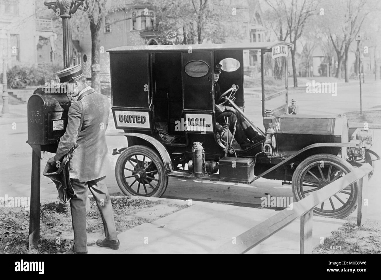 Mailman an Post Box mit seinem Fahrzeug am Strassenrand geparkt Stockfoto