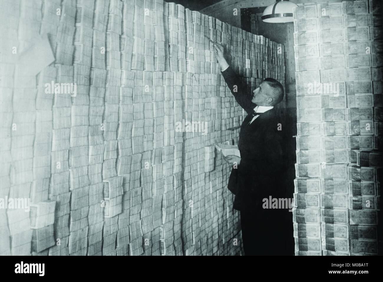 Die Inflation in Weimar Deutschland hat Papiergeld in einer Berliner Bank von Boden bis Decke gestapelt; der Banker zählt Schurken aus gebündelten Banknoten. Stockfoto
