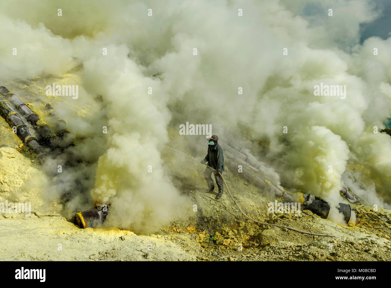 Ranger durch giftige Gase, die versuchen, das überschüssige Rauch aus dem Rohr zu Schwefel erhöht Produktion in Kawah Ijen Berg, Indonesien umgeben Stockfoto