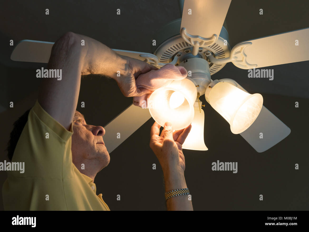 Senior kaukasischen Mann abstauben Lampenschirm in Deckenventilator und Licht Stockfoto