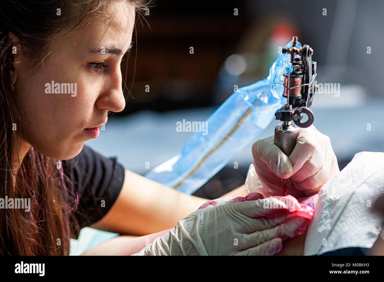 Junge dunkelhaarige Frau tattoo Master, Tattoo von einem kleinen Vogel mit rot Tattoo Maschine, close-up Stockfoto