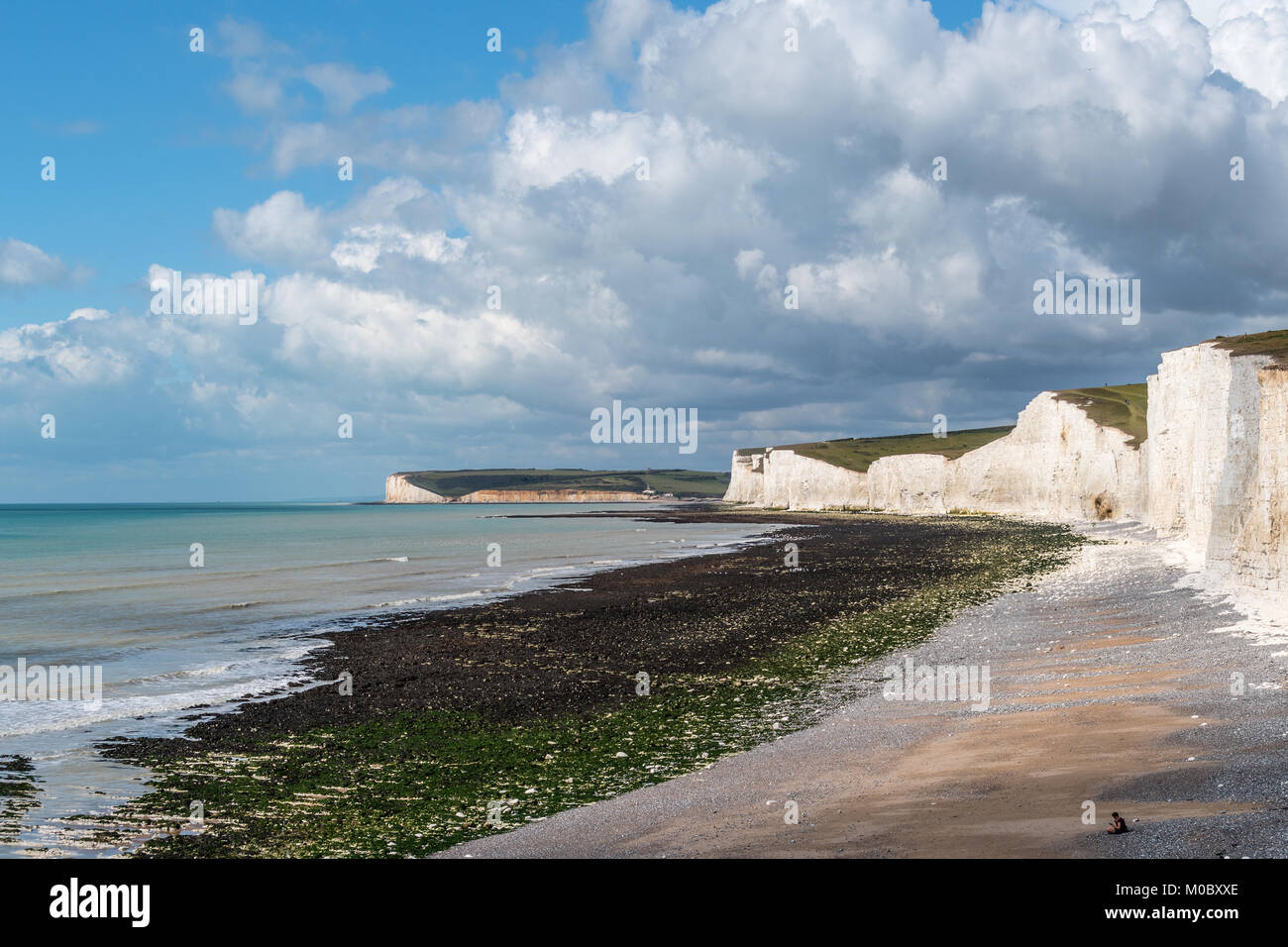 Birling Gap in der Nähe von Beachy Head Sussex. Sieben Schwestern Kreidefelsen mit Sturmwolken über Rollen. Ruhiges Meer mit eingehenden Flut auf Pebble Beach. Sonnigen Tag Stockfoto
