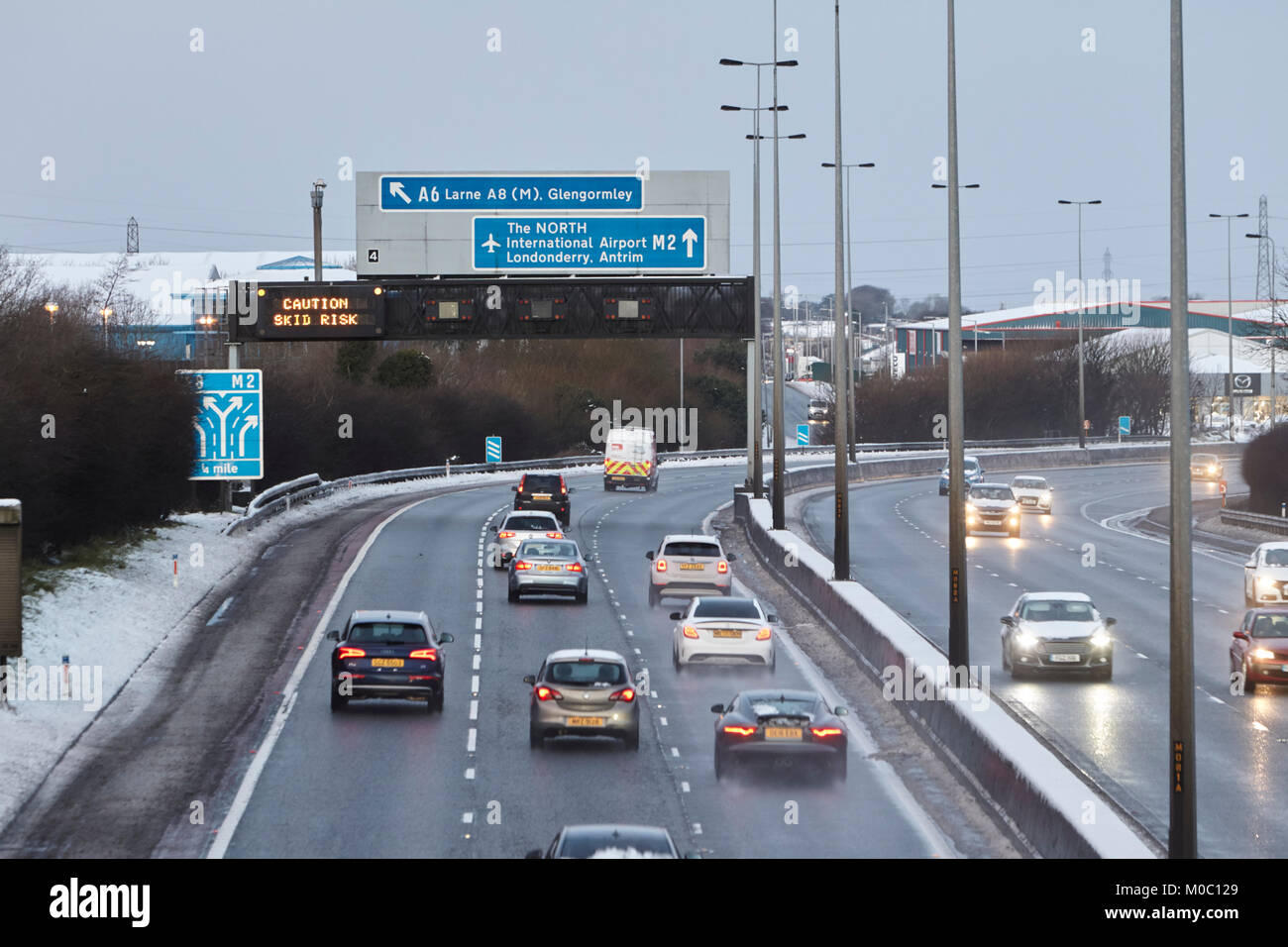 Vorsicht skid Risiko obenliegende gantry Zeichen auf der Autobahn wie Autos entlang knirschte gesalzen Autobahn in Newtownabbey Nordirland Stockfoto