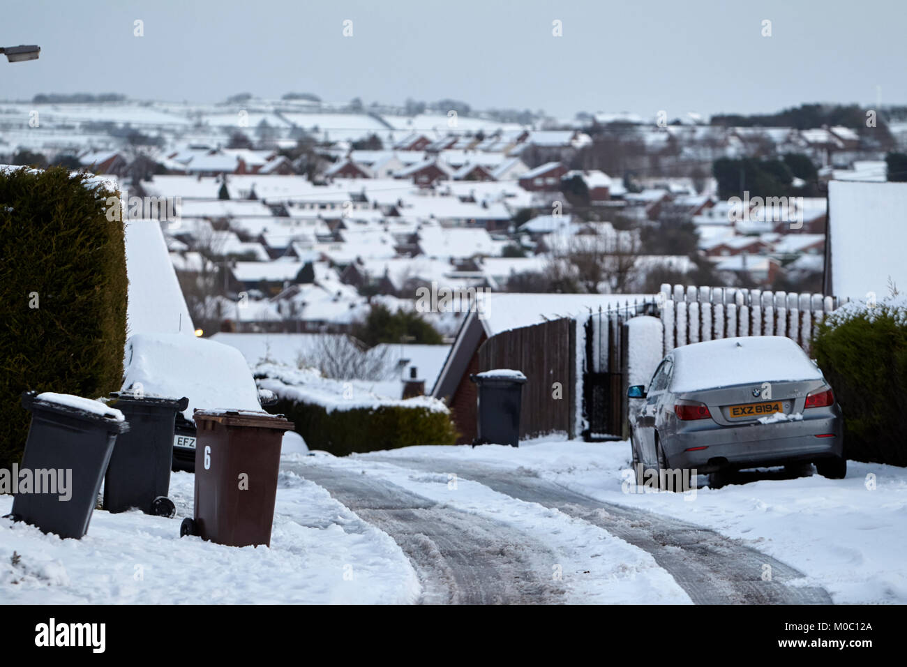 Behälter links und Autos auf Gehwegen geparkt mit klaren Zentrum Vorstadtstraße im Schnee in Newtownabbey Nordirland Stockfoto