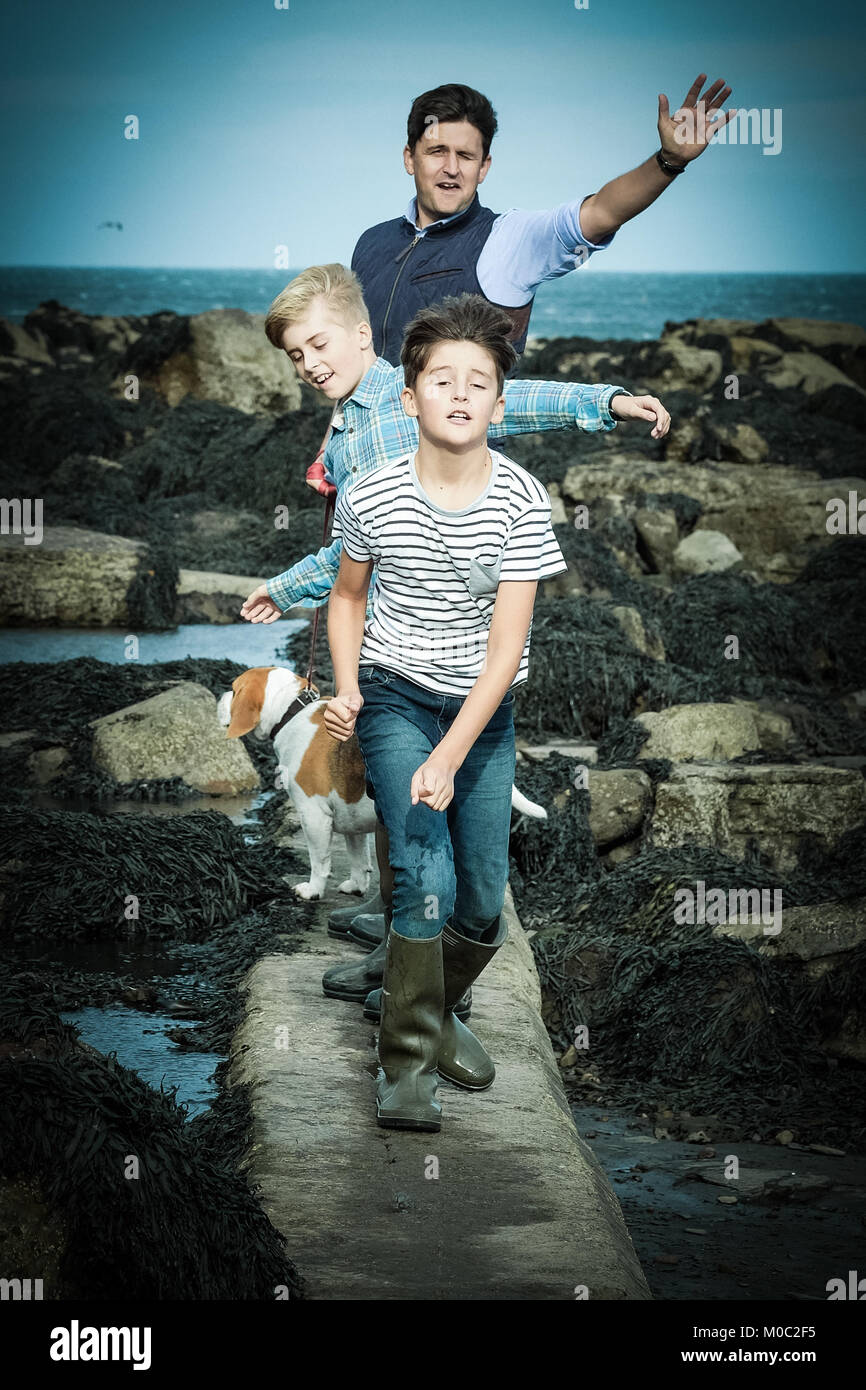 Vater und Söhne, die durch das Meer und Felsen Pools in [Songbook] Bay, Yorkshire, Großbritannien Stockfoto