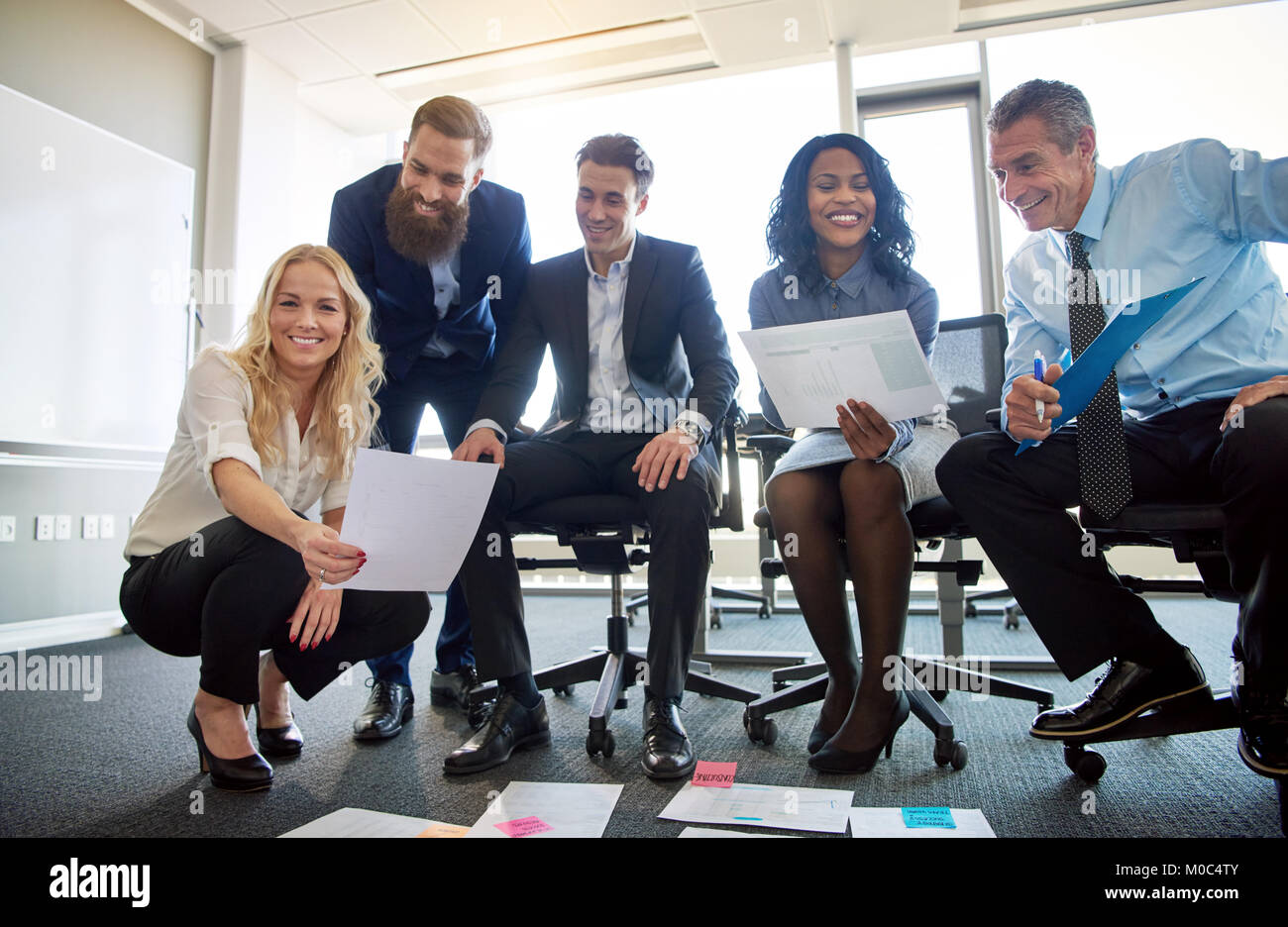 Porträt einer vielfältigen Gruppe von lächelnden Führungskräfte gemeinsam Brainstorming mit Dateien, die auf dem Boden eines modernen Büros festgelegt Stockfoto