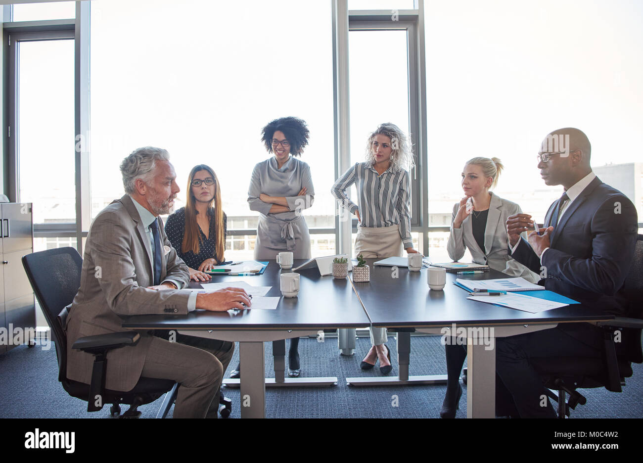Vielfältige Gruppe von Führungskräften zusammen gesprochen um einen Tisch während einer Sitzung in einem hellen modernen Büro Stockfoto