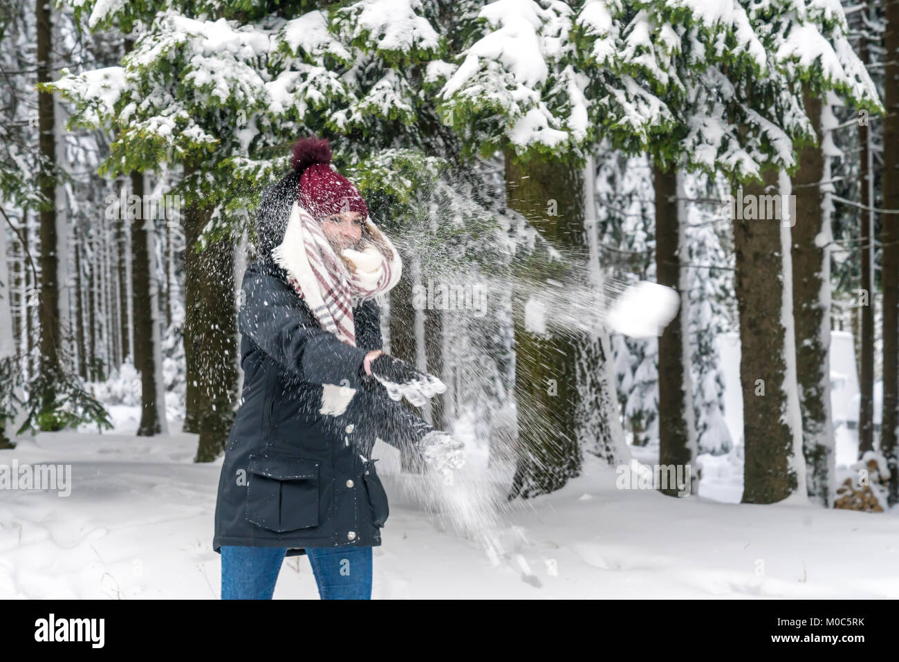 Eine glückliche junge Frau wirft einen Schneeball in den Wald Stockfoto