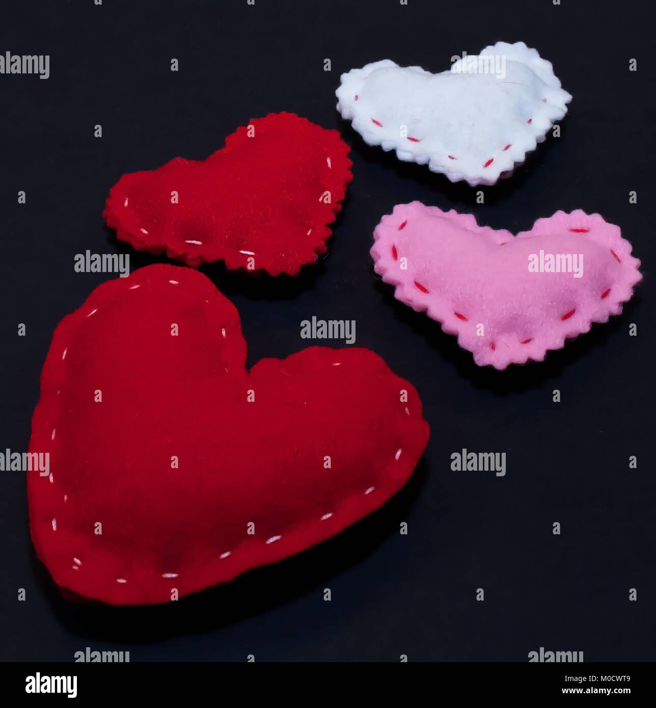 Vier Herzen, drei kleinere, rot, weiß und rosa zusammen mit einem größeren Rotes auf schwarzem Hintergrund Stockfoto