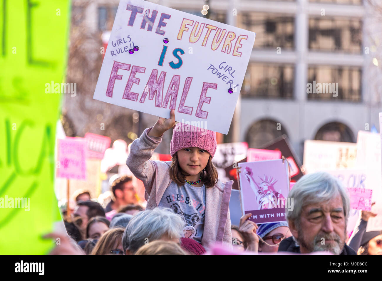 San Francisco, Kalifornien, USA. 20. Januar, 2018. Die 2018 Frauen März in San Francisco, von der Frau März Bay Area organisiert. Ein junges Mädchen, das Reiten auf den Schultern über die Masse nach unten marschieren Market Street hält ein Schild mit der Aufschrift, "Die Zukunft ist weiblich. Girl Power!' Sie mit Entschlossenheit in die Kamera schaut. Stockfoto