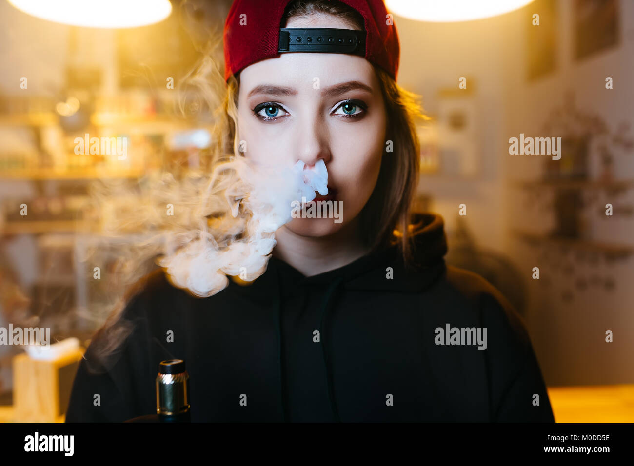 Junge hübsche Frau in Rot cap Rauch eine elektronische Zigarette am vape Shop. Hip Hop Style. Nahaufnahme. Stockfoto