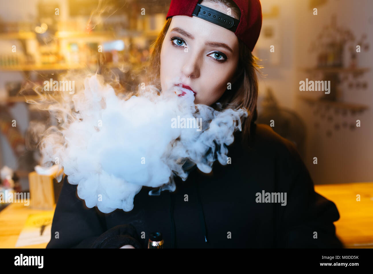 Junge hübsche Frau in Rot cap Rauch eine elektronische Zigarette am vape Shop. Hip Hop Style. Nahaufnahme. Stockfoto