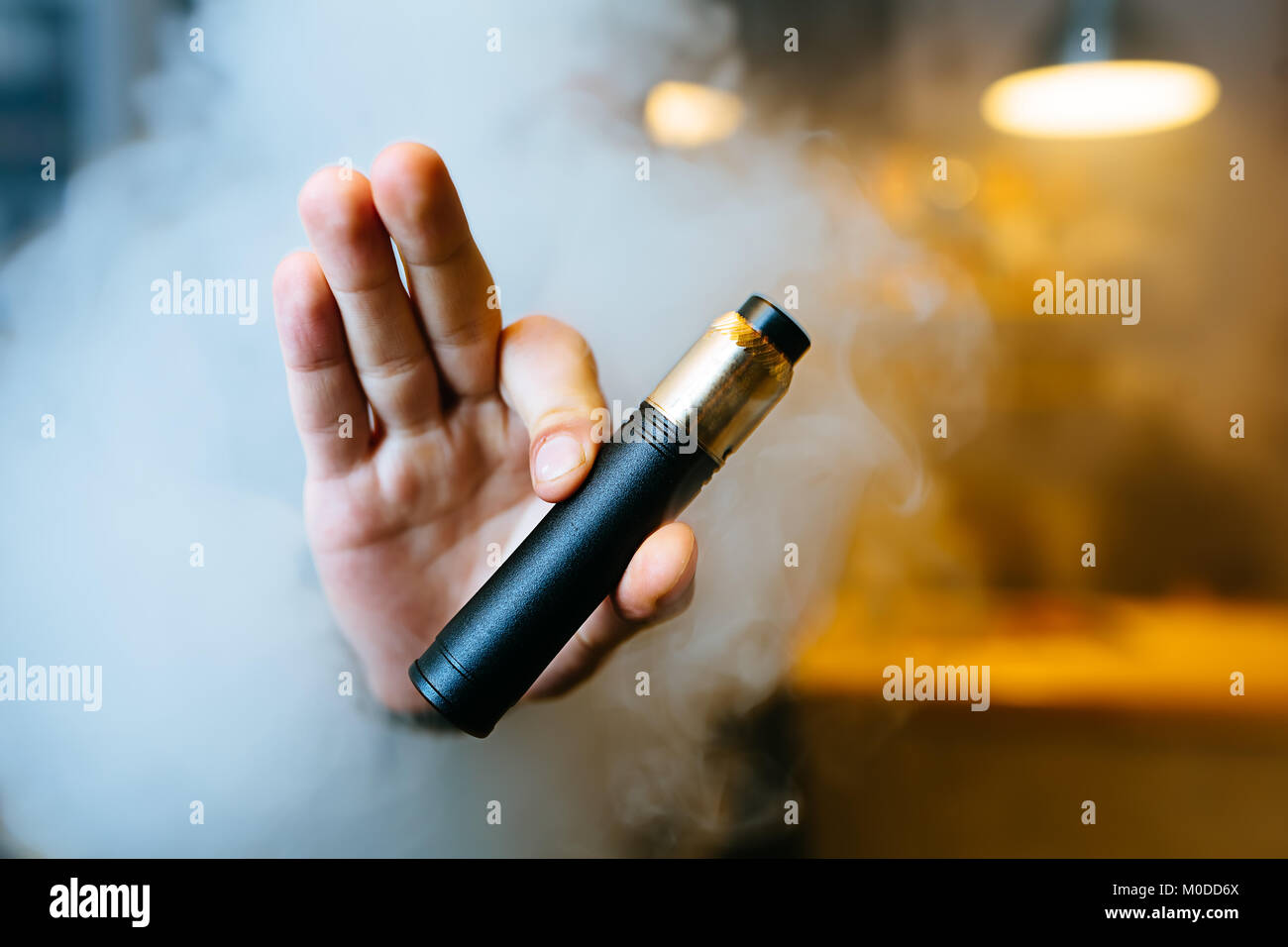 Junge Bart man show vaping Gerät auf seiner ausgestreckten Hand durch eine Wolke aus Dampf. Selektive konzentrieren. Vaping Konzept. Kopieren Sie Platz. Stockfoto