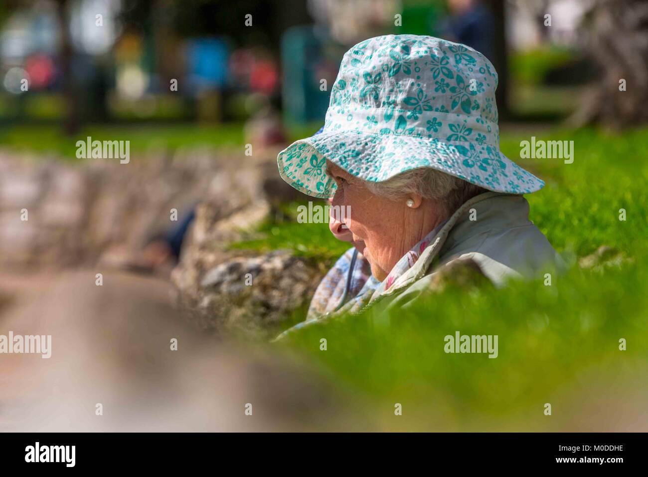 Eine alte Dame im Ruhestand, in der Sonne zu sitzen mit Ihren Sonnenhut auf. Stockfoto