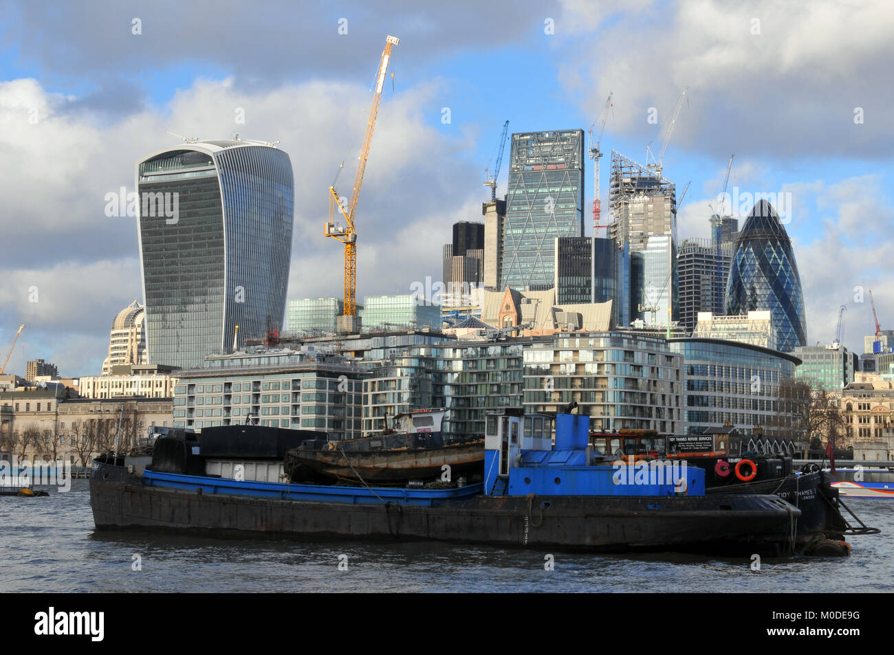 Eine alte Arbeiten Thames River Boot vor der finanziellen Herzen der Stadt mit der berühmten Skyline einschließlich aller bekannten Gebäuden vertäut. Stockfoto