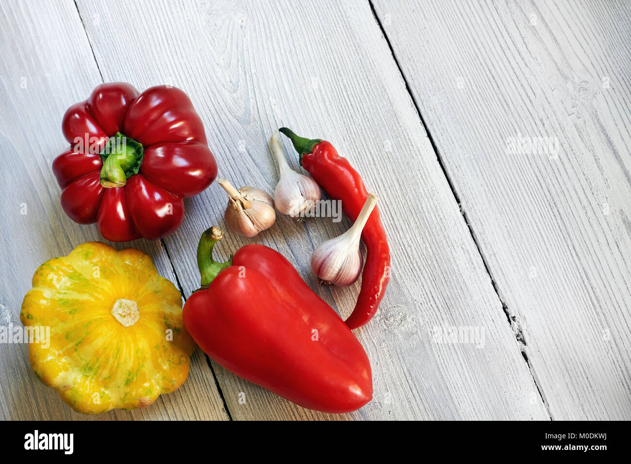 Rote, gelbe und grüne Bush, Kürbisse, Paprika, auf weißem Holz Hintergrund Knoblauch. Garten, Agrar- und Landwirtschaft Konzept. Stockfoto