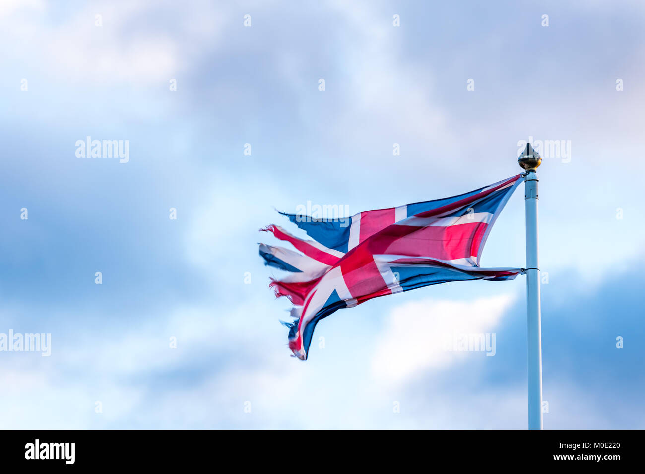 Britische Flagge mit zerrissenen Rändern wellenartig über bewölkten Himmel. Stockfoto