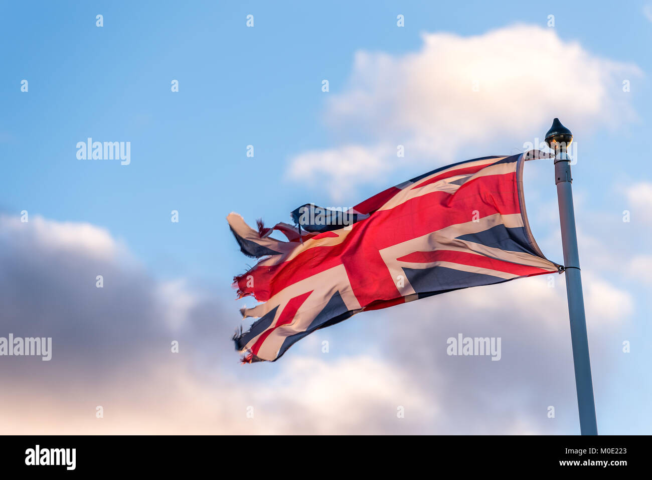 Britische Flagge mit zerrissenen Rändern wellenartig über bewölkten Himmel. Stockfoto