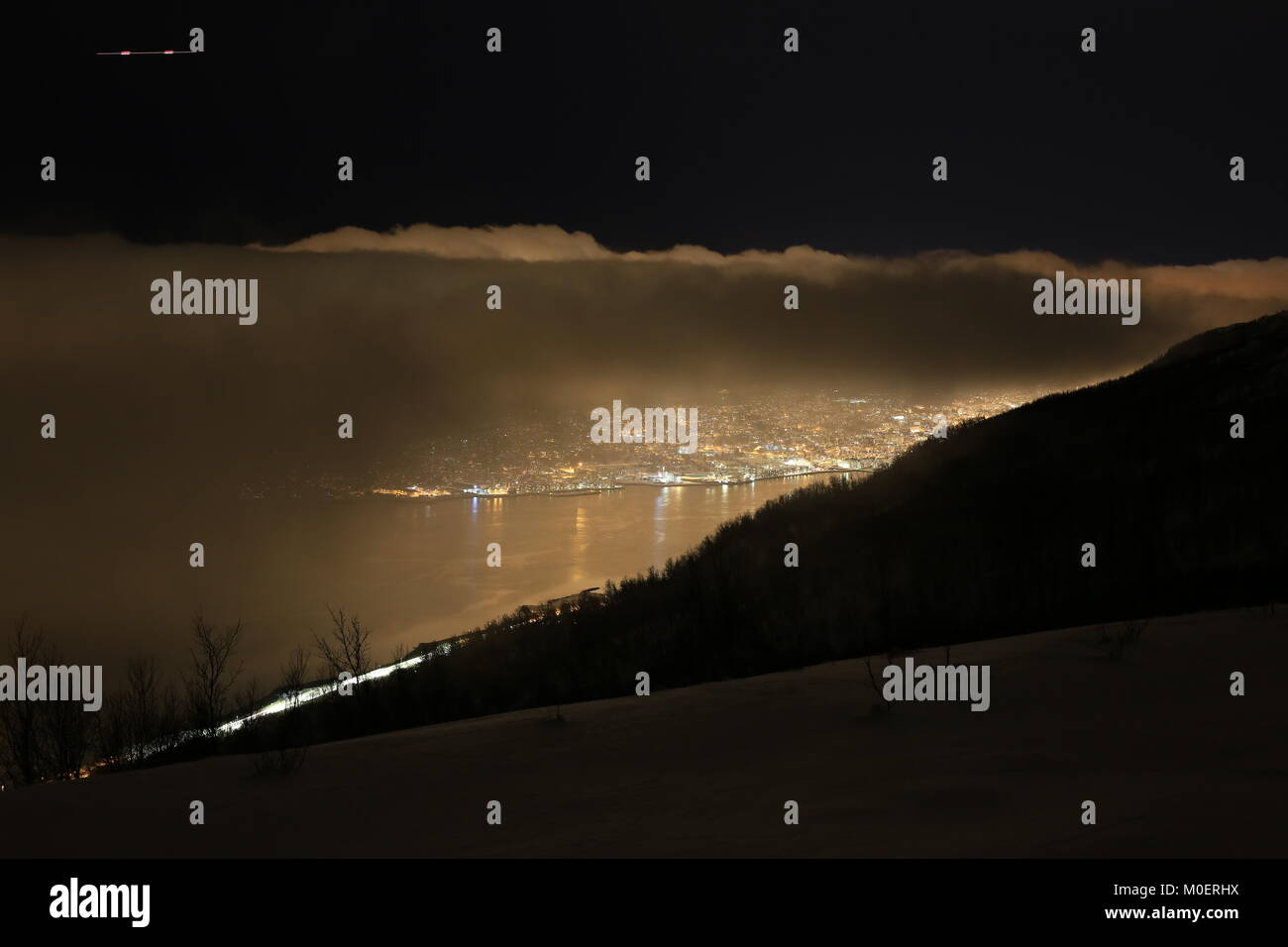 Die Lichter der Stadt Tromsö scheint durch die Wolken Stockfoto