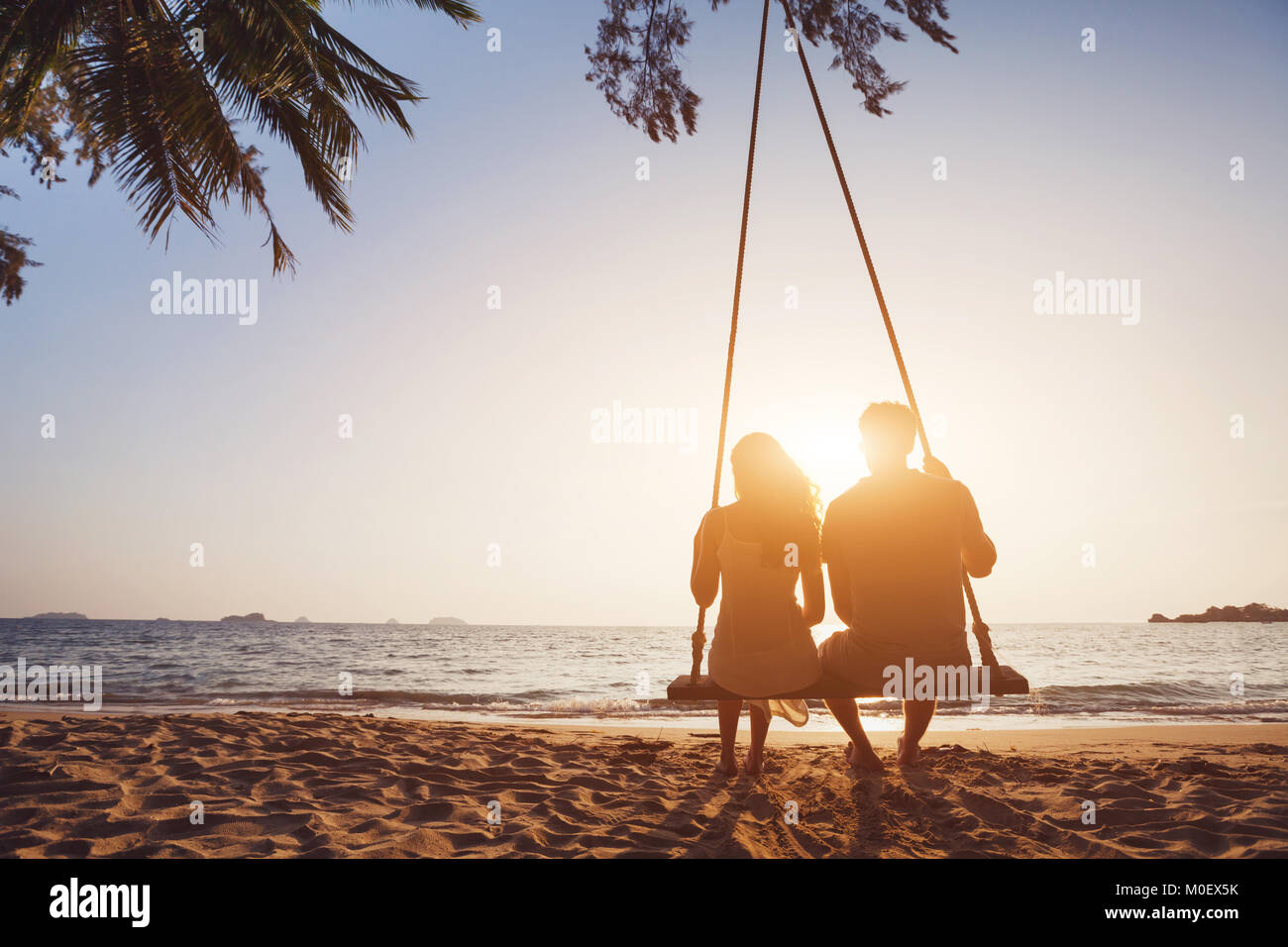 Romantisches Paar in Liebe sitzen zusammen am Seil schwingen am sunset beach, Silhouetten von jungen Mann und Frau auf Urlaub oder Flitterwochen Stockfoto